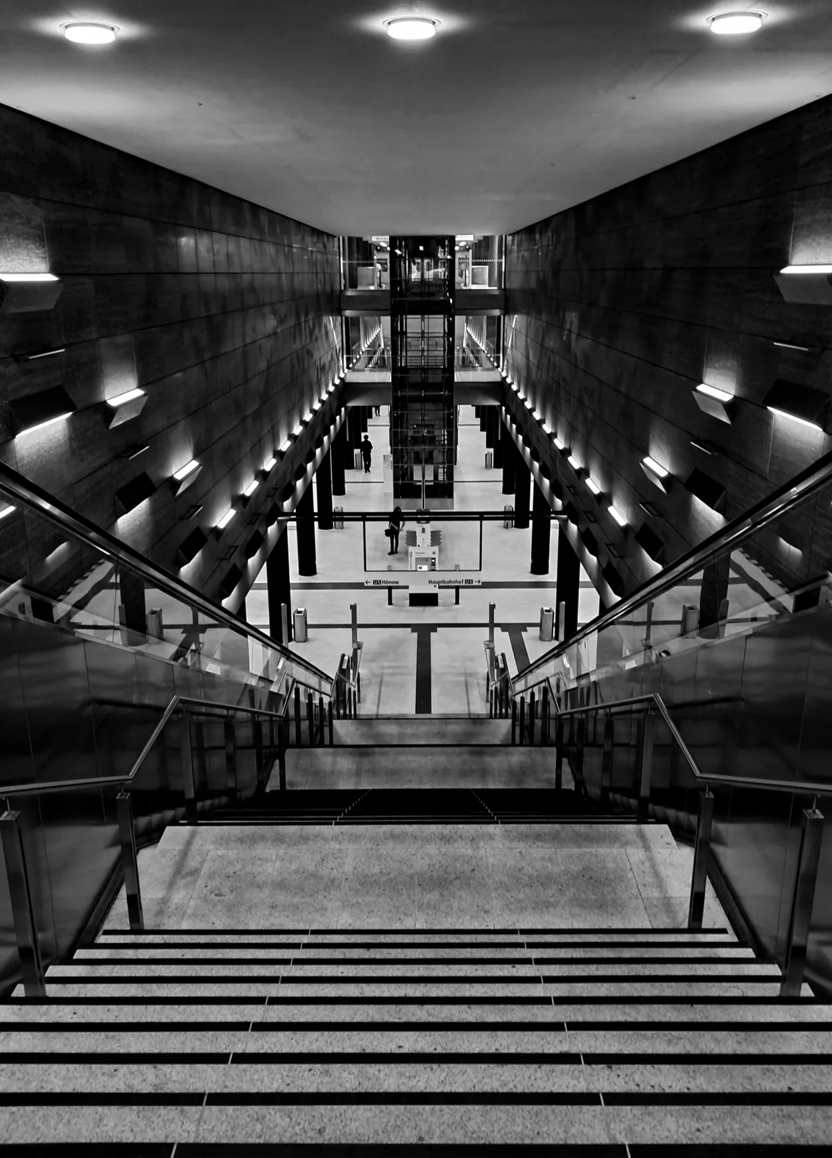 Wide stair descending into a lit underground hall, symmetrical railings
