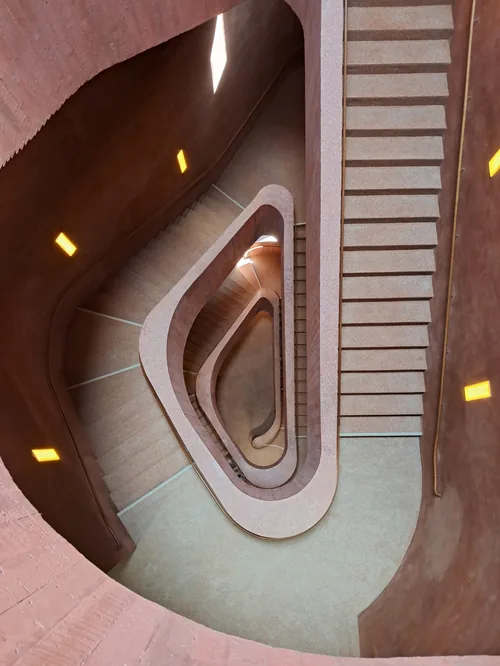 Oval stairwell from above in warm pink plaster, small lights in the walls