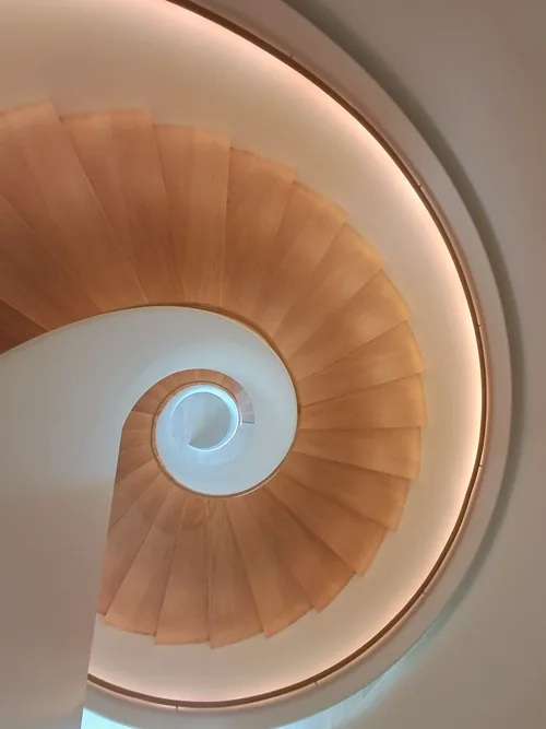 Spiral stair from below in warm orange, coiling toward a pale oculus