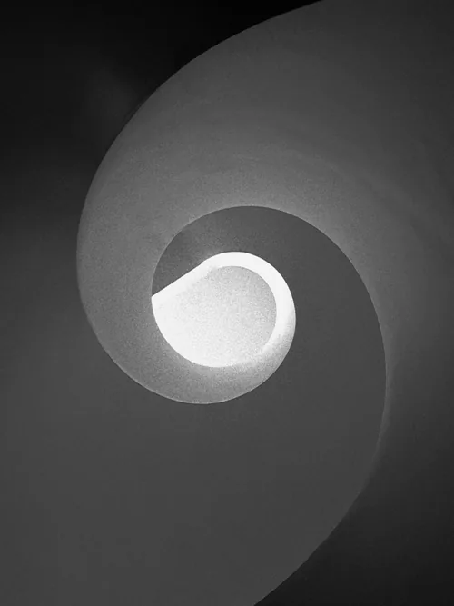 Grey spiral stair winding around a bright, egg-shaped opening