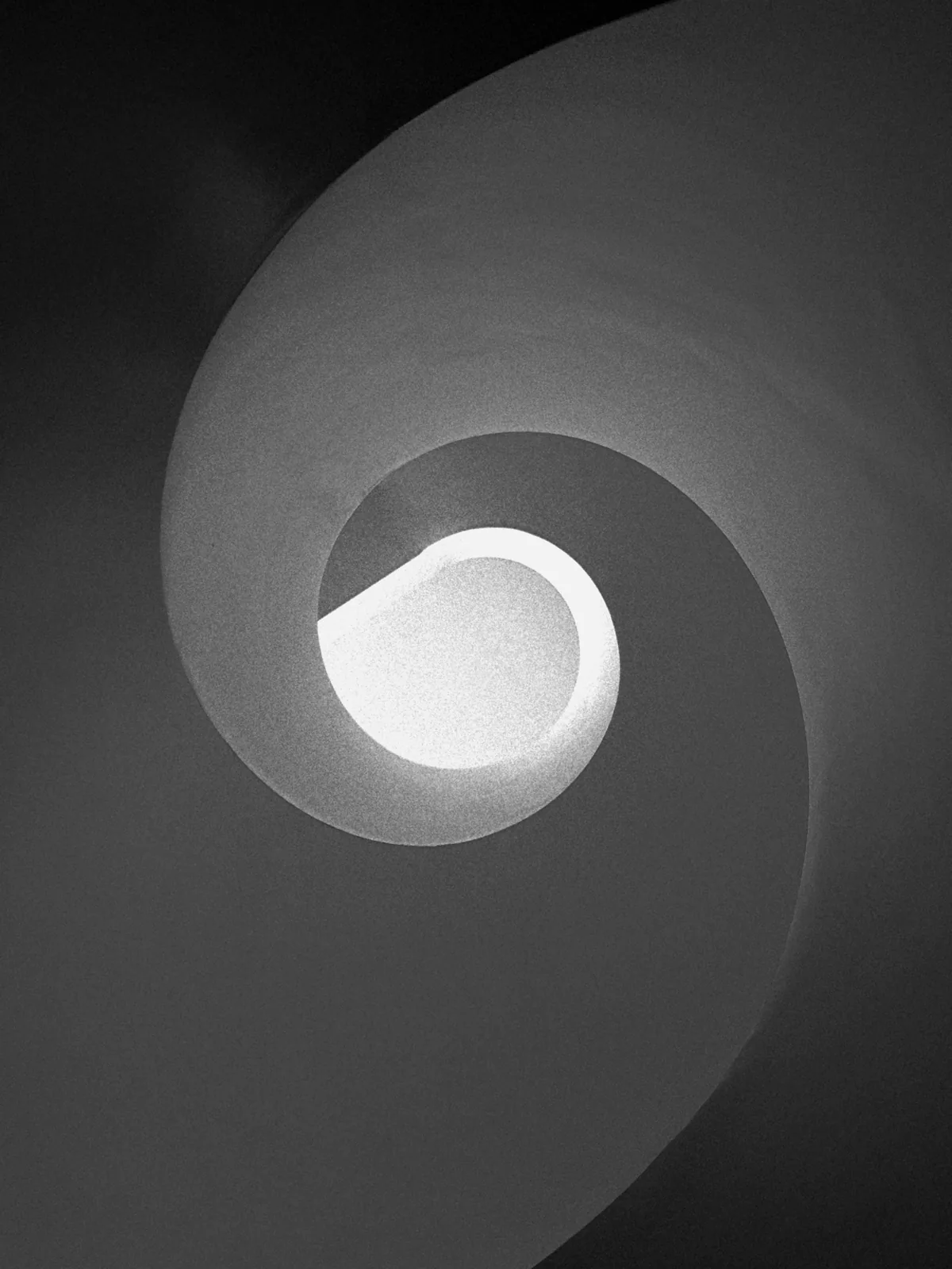 Grey spiral stair winding around a bright, egg-shaped opening
