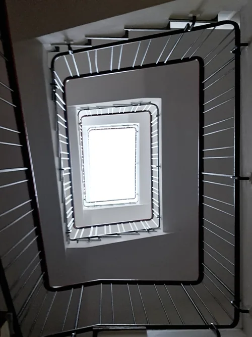 Square stairwell from below, flights wrapping a bright skylight