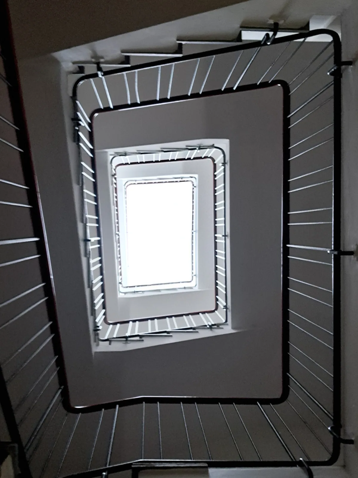 Square stairwell from below, flights wrapping a bright skylight