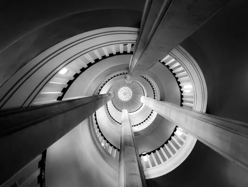 Looking up through a round stairwell, beams converging on a white eye