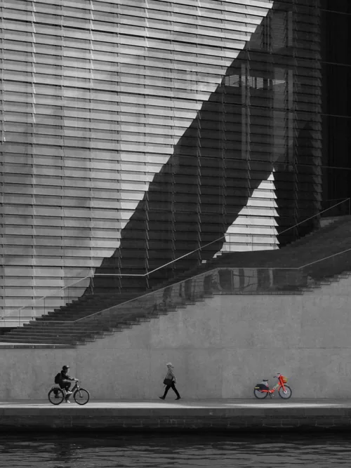Diagonal stair shadow across a striped façade, cyclists passing below