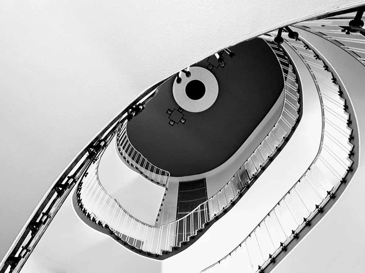 Oval stairwell from below, white rail curving around a black eye