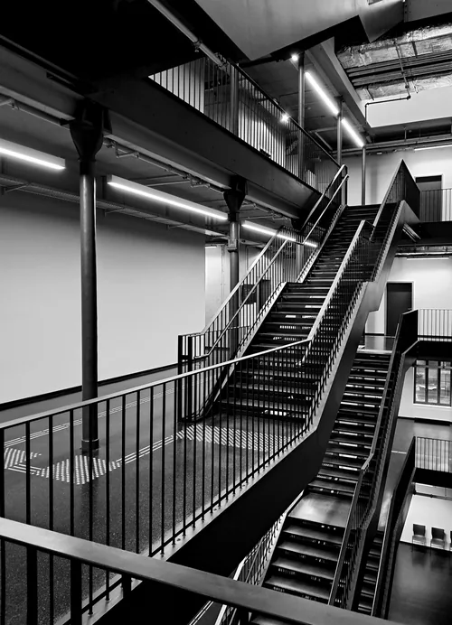 Industrial steel stairs climbing through a tall black-and-white hall