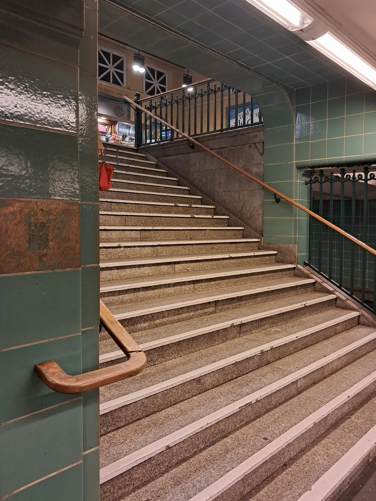 Tiled stair rising in an old station passage, brass handrail