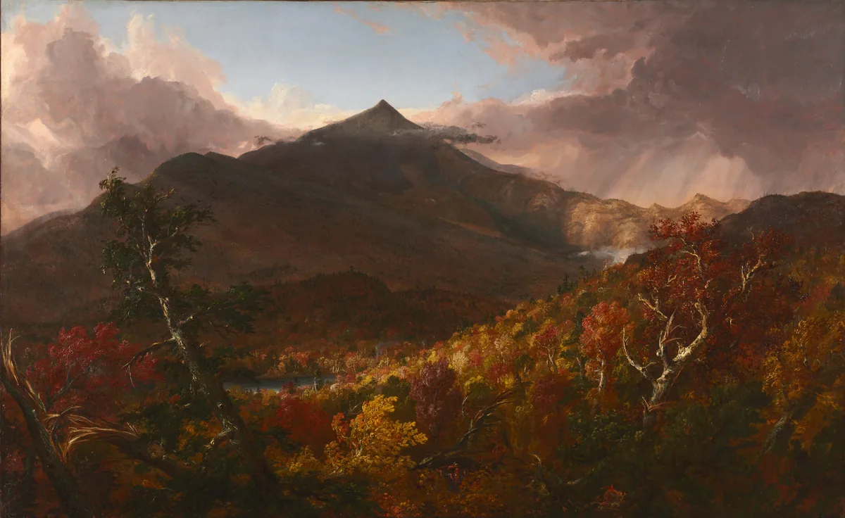 A dark peak rises above a forest blazing in autumn red and gold, storm clouds lifting from the summit.