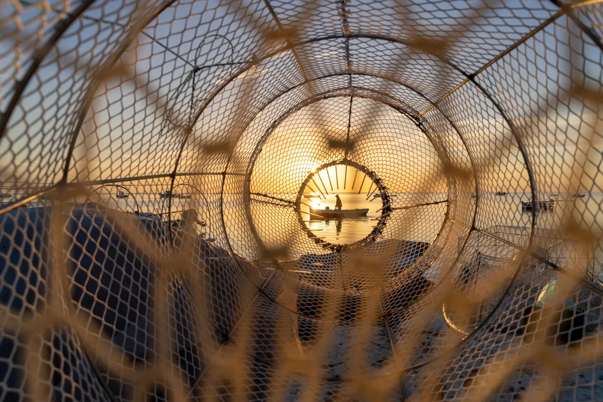 A fisherman returns to the port at daybreak in Kerkennah, as seen through a fish trap - wide view - Tunisia