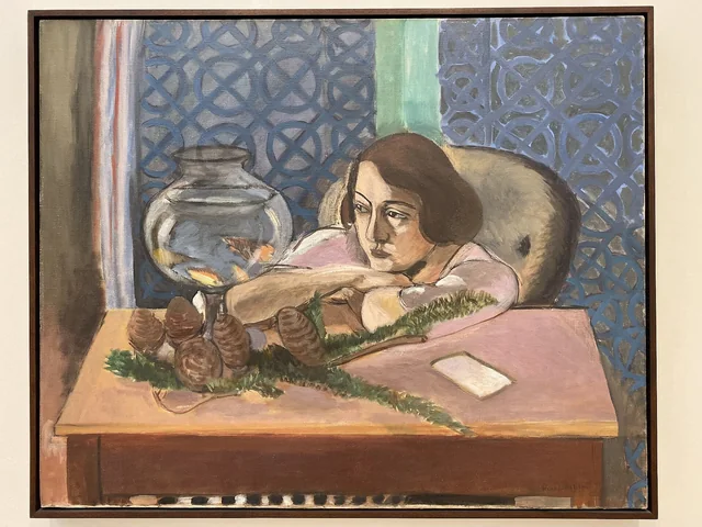 Painting of woman, arms crossed on brown desk, staring at goldfish.