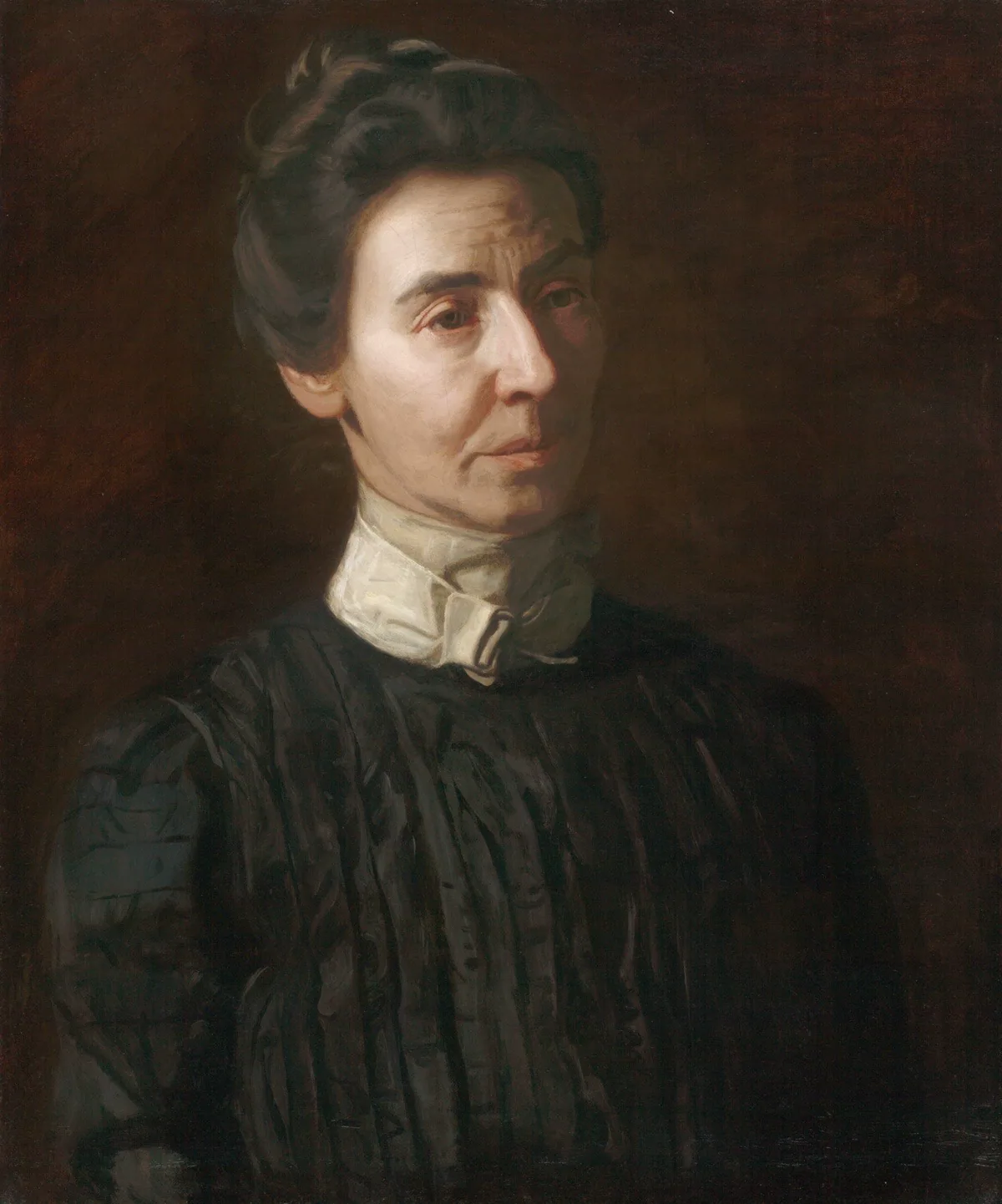 Dark portrait of an older light-skinned women with dark hair in a black dress and white collar, her hair pinned up. Her face is in partial shadow.