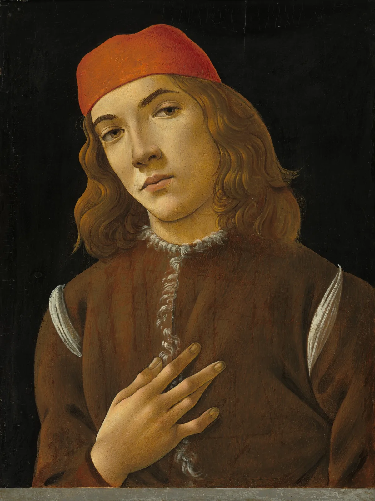 This vertical portrait shows the head, shoulders, and chest of a young man with smooth, pale skin and shoulder-length, dark blond hair positioned behind a narrow gray, stone ledge.