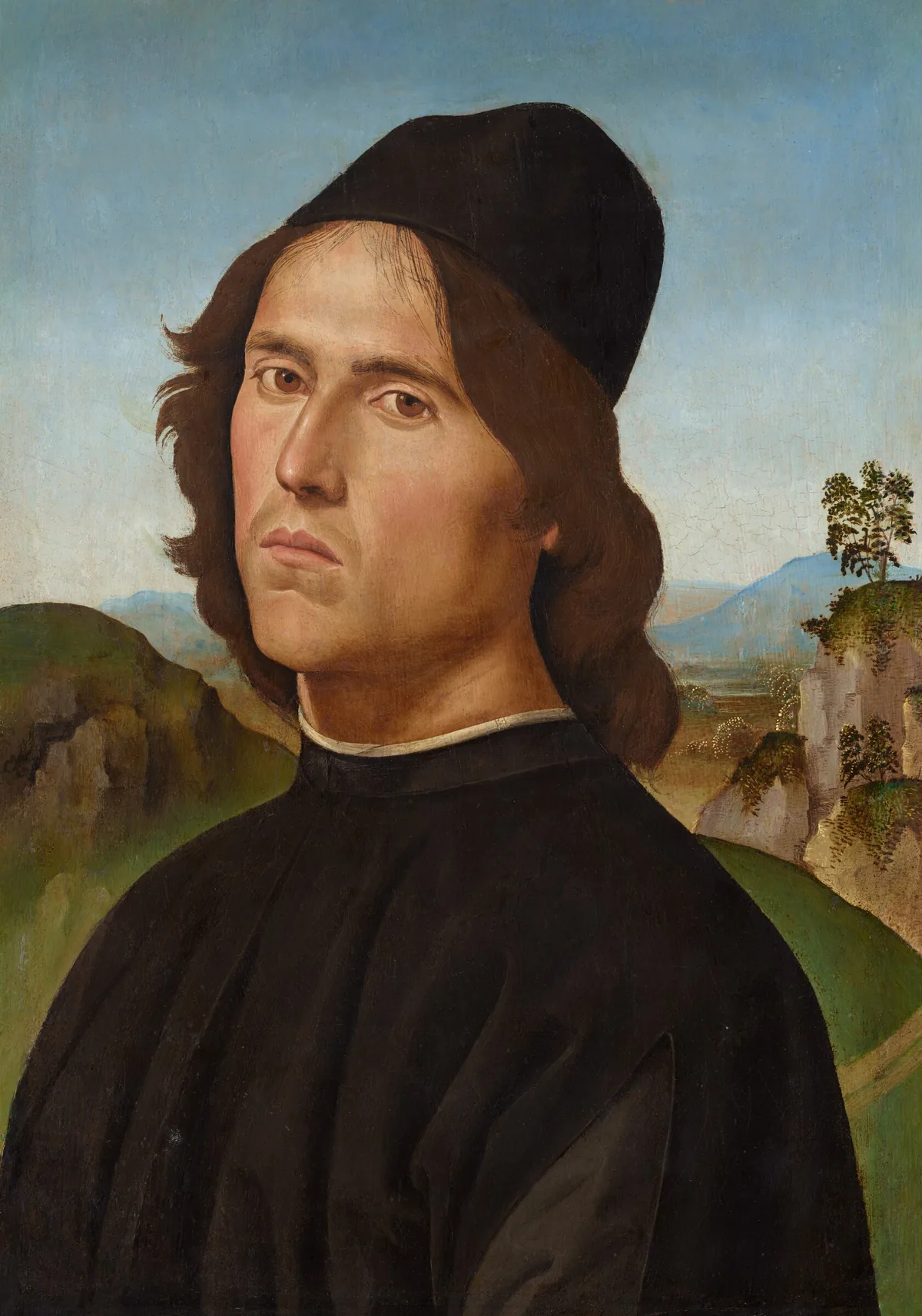 Shown from the chest up, a pale-skinned man with a narrow face looks at us from in front of a distant landscape in this vertical portrait painting.