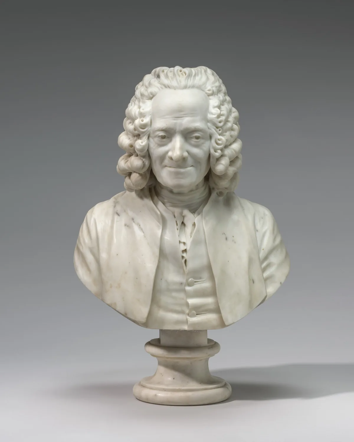 The head, shoulders, and upper chest of a man wearing a curly wig are carved from white marble in this freestanding portrait sculpture.
