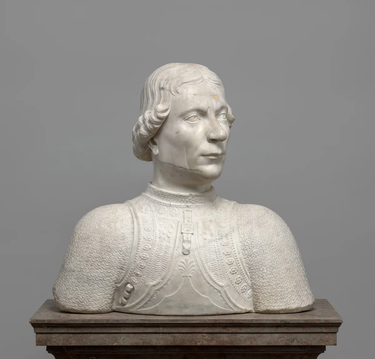 The head and shoulders of a cleanshaven man are carved from white marble lightly streaked in gray in this freestanding sculpture.
