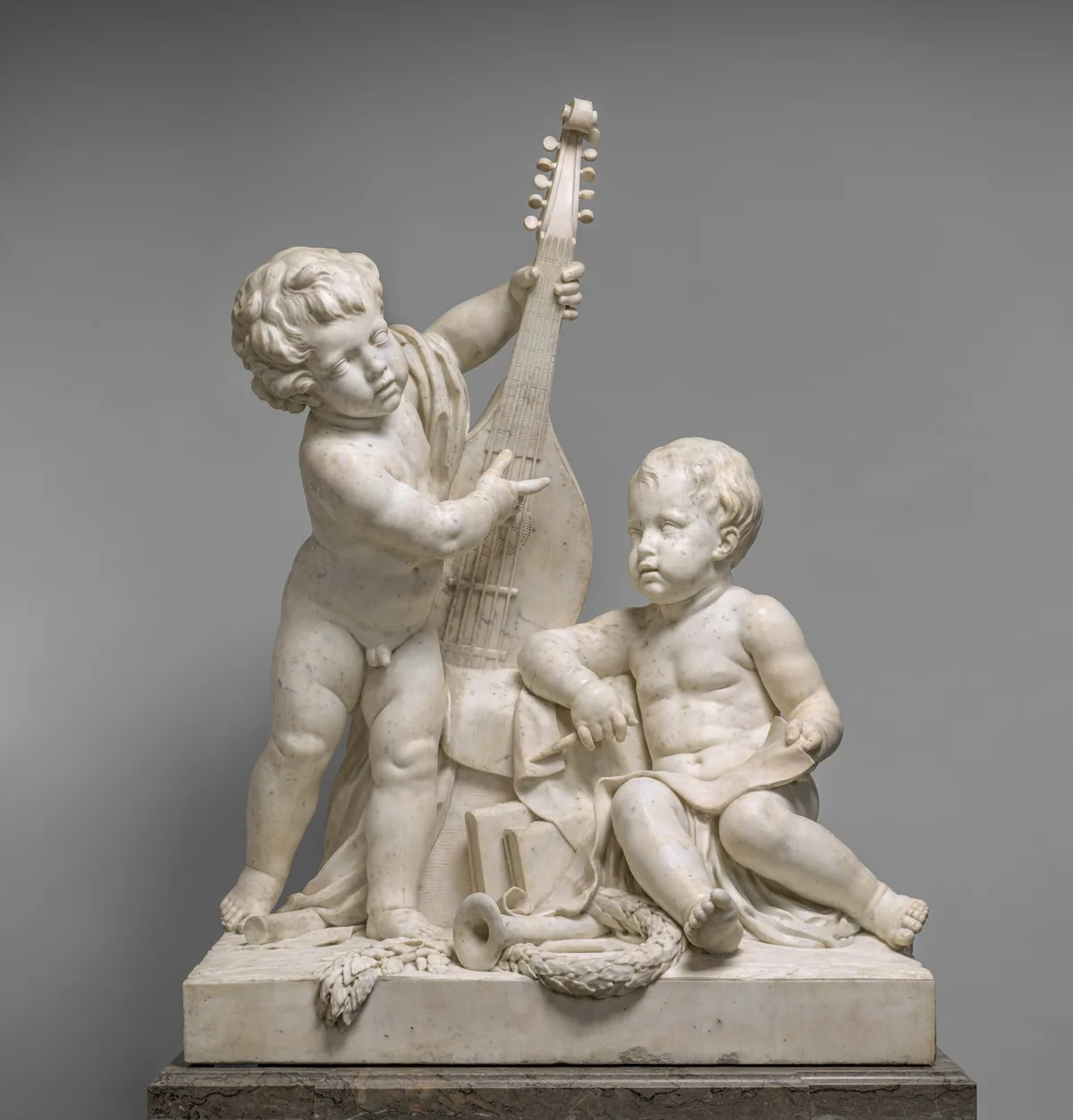 The sculpture features two cherubic children interacting with musical instruments and art materials.