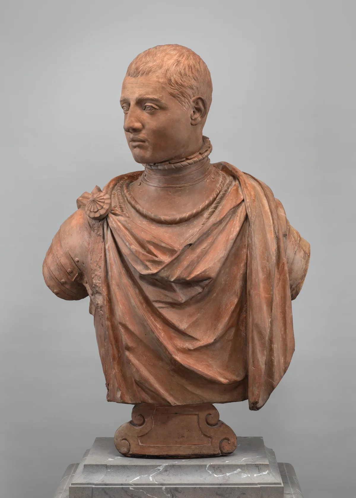 The sculpture depicts a man's bust with short hair, dressed in a draped garment featuring a shell-shaped decoration on his right shoulder.
