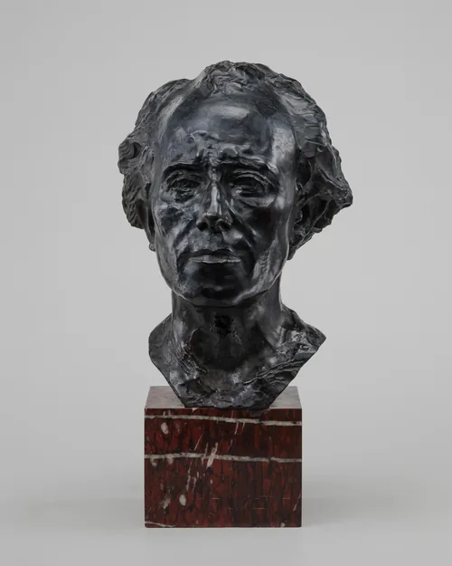 Cast in bronze, this freestanding sculpture shows the head and neck of a man with wavy hair and a deeply lined face.