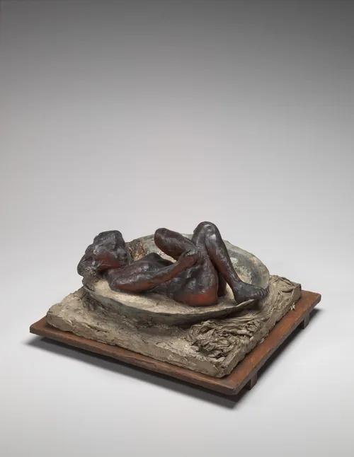 The sculpture depicts a nude woman lying in a shallow, oval basin with bent legs, grabbing one of her feet in her hand while the other foot rests on the rim of the basin.