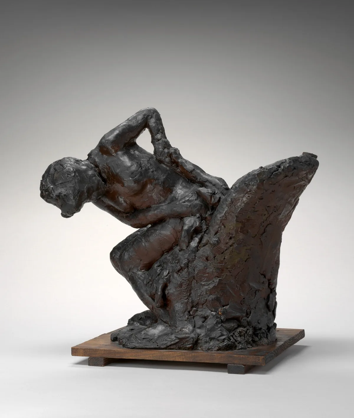 The sculpture depicts a human figure crouched with one knee bent and the other leg extended forward.