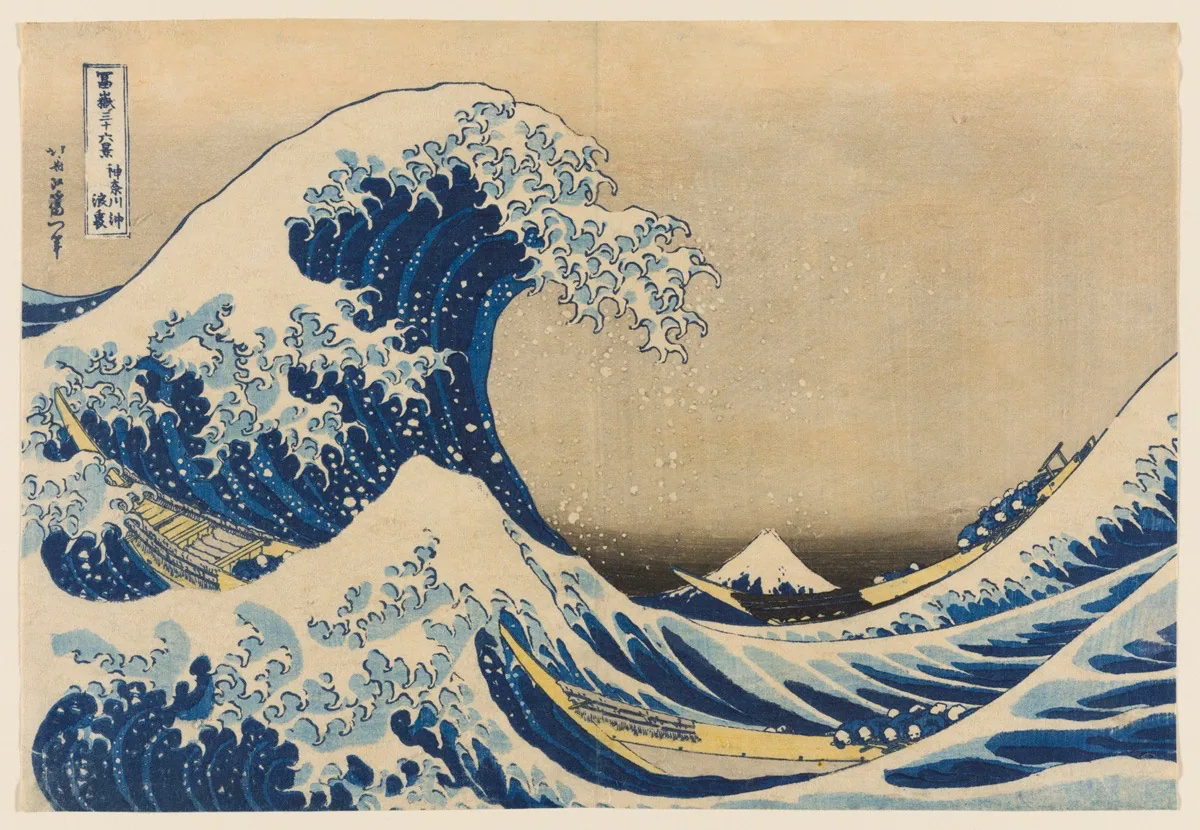 A color woodblock print of a large crashing wave, looms over two narrow boats full of people. Mt Fuji in the background.  There is a faint peach colored sky.