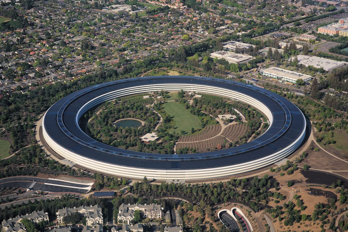 The continuous glass ring of Apple Park seen from the air, enclosing a planted courtyard.