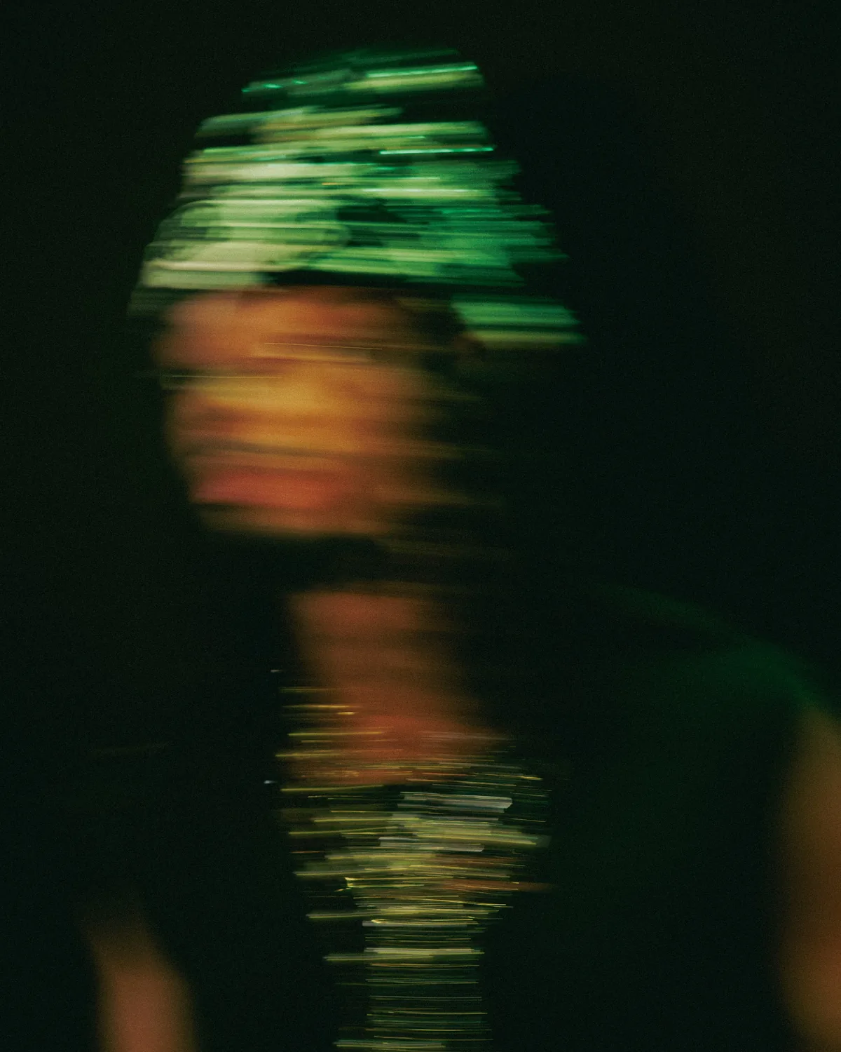 A face dissolves into streaks of green and amber light in a long-exposure experiment.