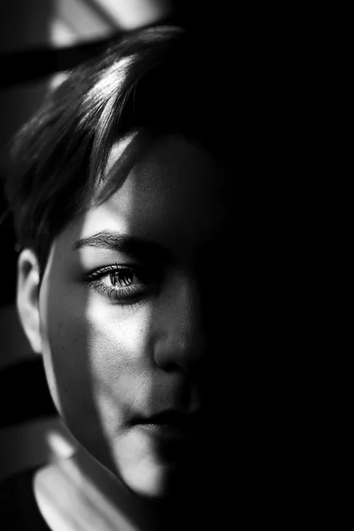Half a face caught in a blade of window light, the other half lost to shadow.
