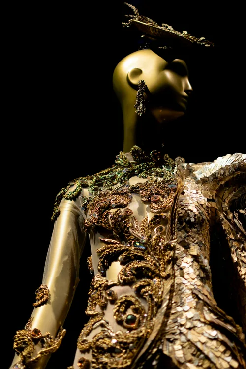 A mannequin dressed in a hand-embroidered gold gown, photographed close, like a reliquary.
