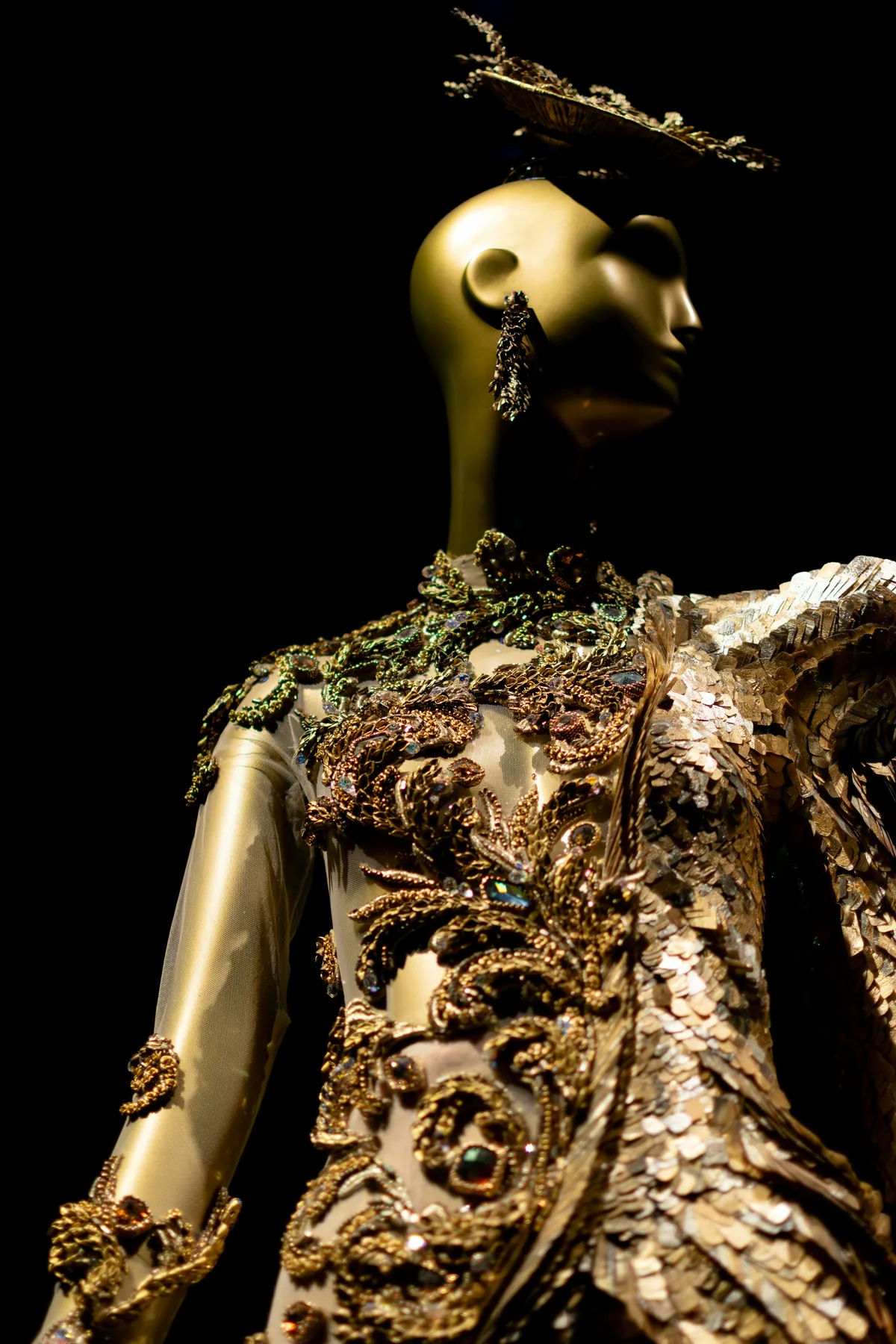 A mannequin dressed in a hand-embroidered gold gown, photographed close, like a reliquary.
