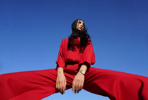 A portrait shot low against a clear blue sky, the subject in a matching red set, shot from below.