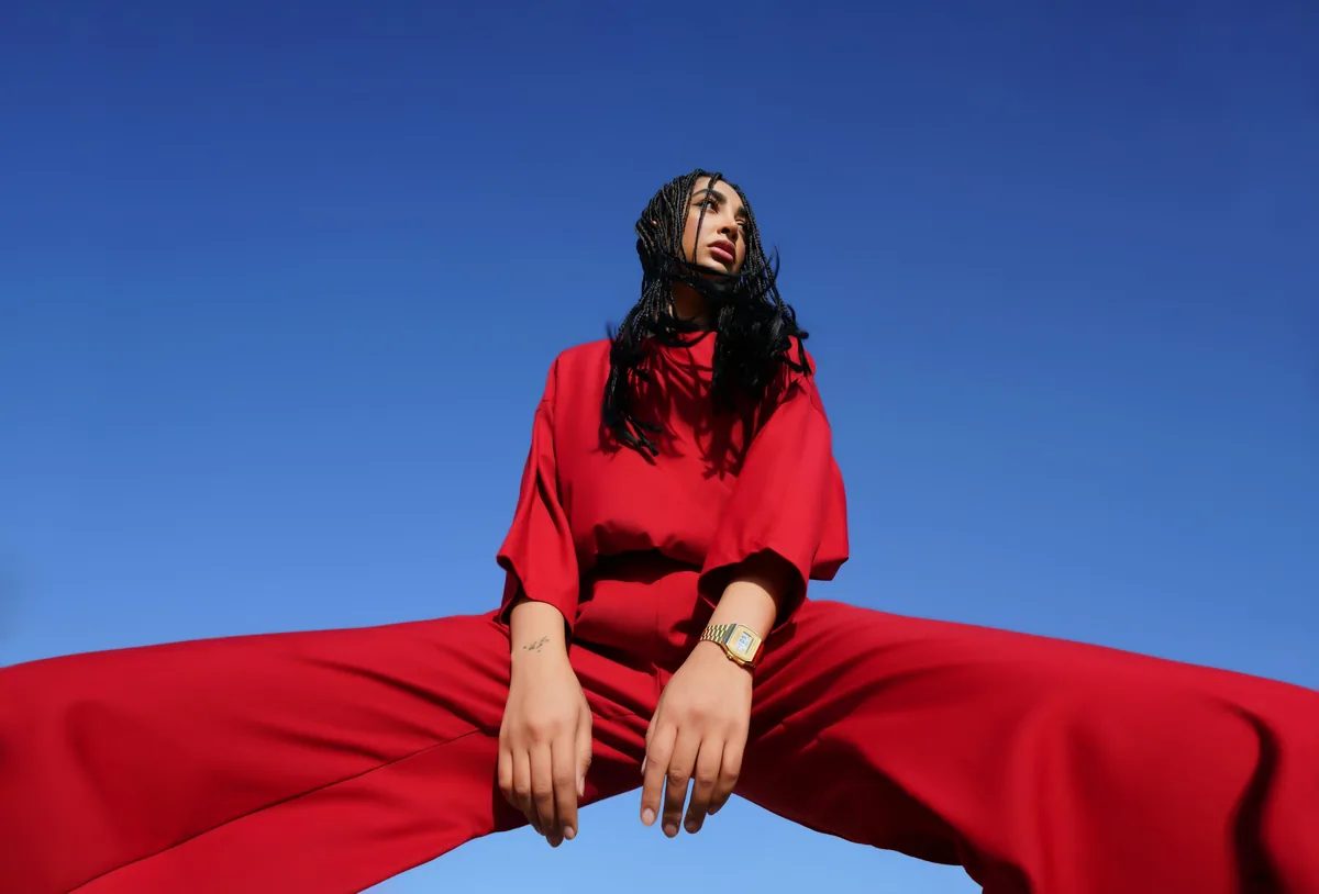 A portrait shot low against a clear blue sky, the subject in a matching red set, shot from below.