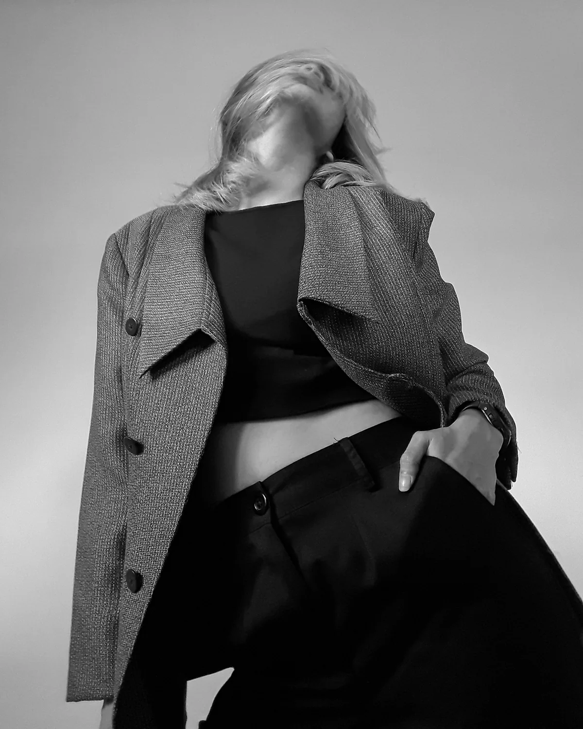 A black-and-white study of tailoring: a hand pushed into a trouser pocket, the face lost in motion-blurred hair.