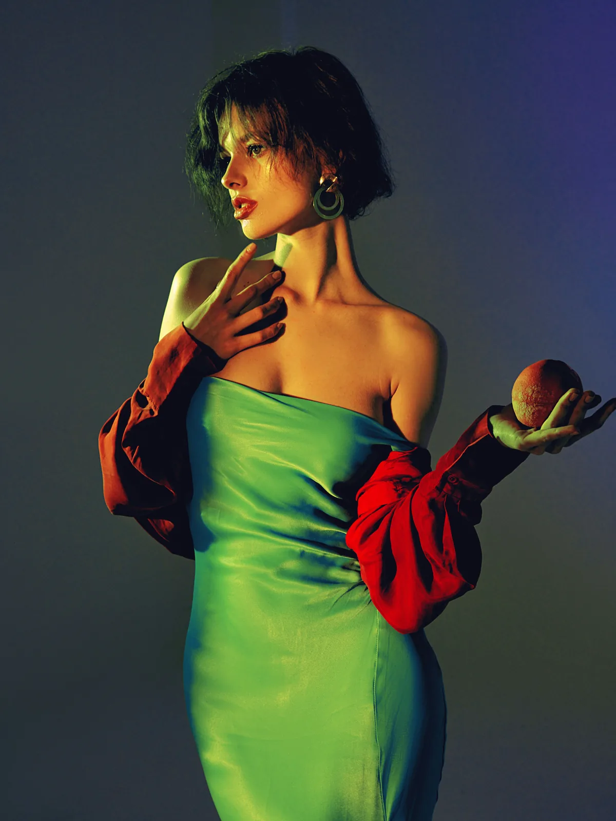 A two-colour lighting study: green dress under green light, a red sleeve and a held apple lit separately in red.