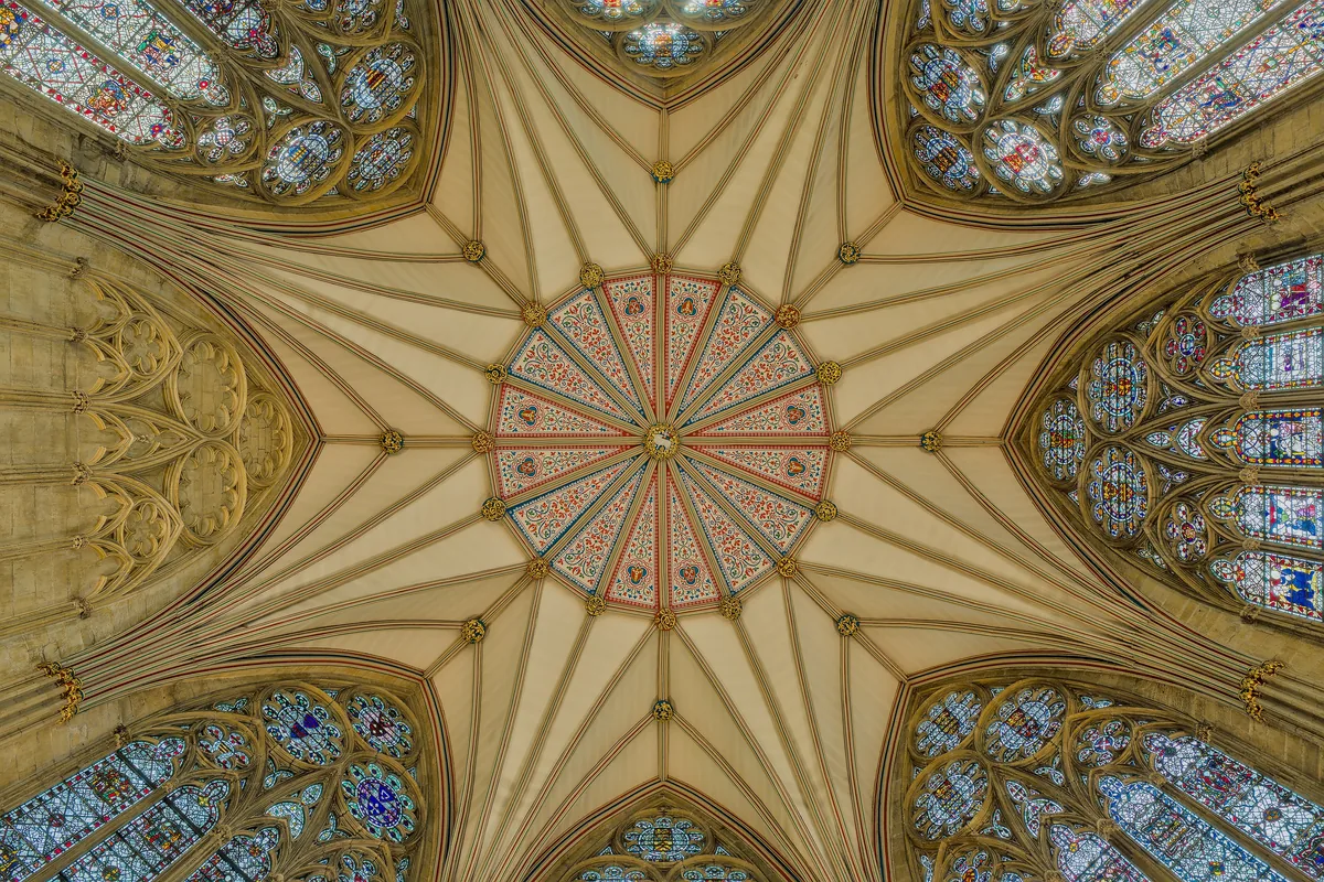 Looking straight up into the star-shaped timber vault of the chapter house at York Minster, ringed by stained glass.