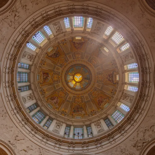 The coffered dome of Berlin Cathedral seen from directly below, a ring of windows around a golden oculus.