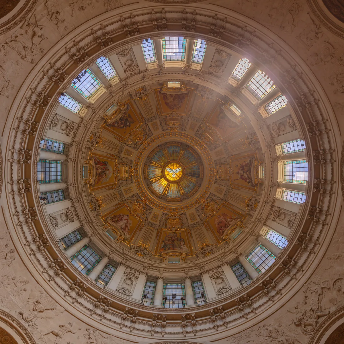 The coffered dome of Berlin Cathedral seen from directly below, a ring of windows around a golden oculus.