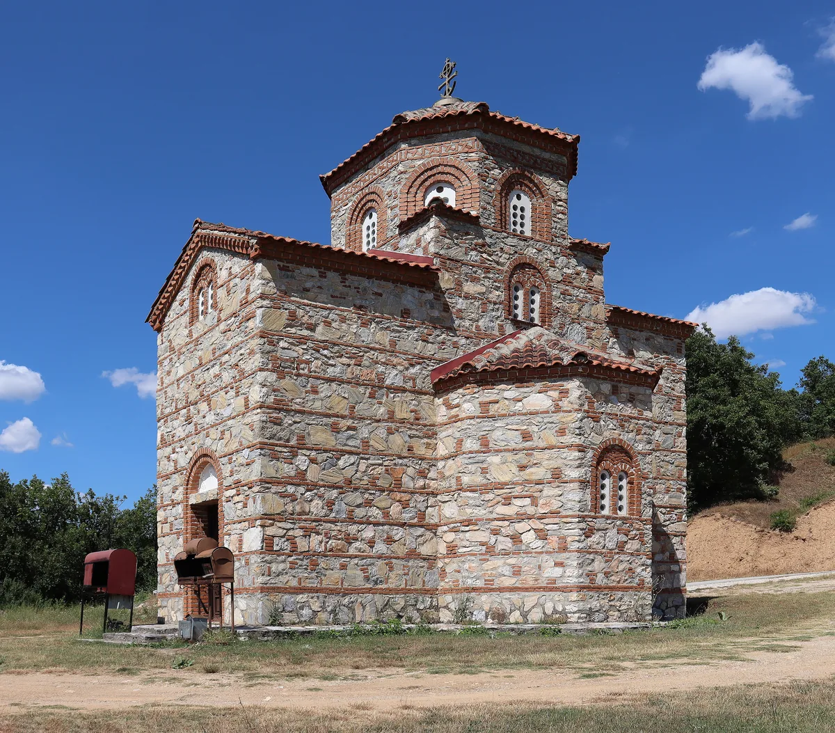 A small Byzantine-style church of banded stone and brick under a clear summer sky.
