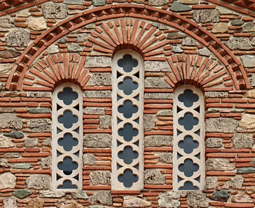 A triple window of carved stone lattices set in a wall of alternating brick and stone.