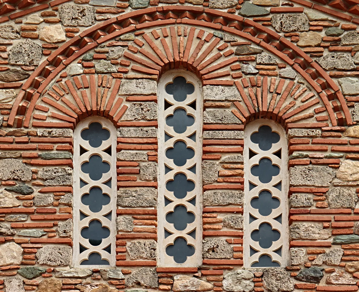 A triple window of carved stone lattices set in a wall of alternating brick and stone.