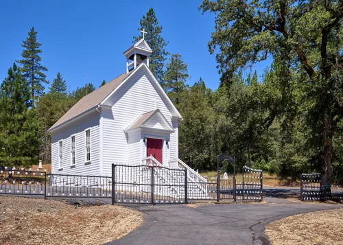 A small white clapboard mission church with a bell cupola among pines and oaks.