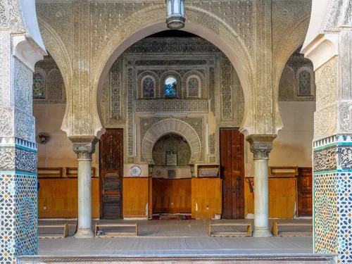 The prayer hall of the Bou Inania madrasa: carved stucco arches, cedar doors and zellige tile around the mihrab.