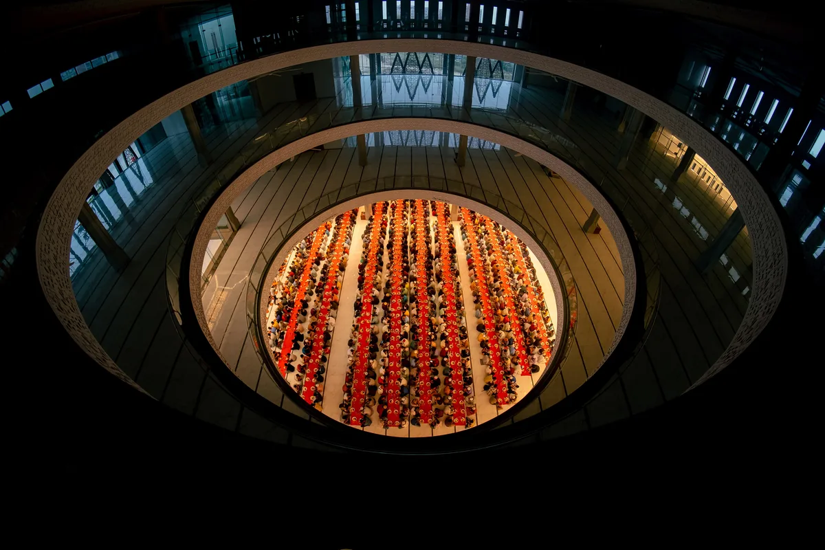 Seen from the gallery above, long rows of worshippers break the Ramadan fast on a round floor under a ring of balconies.