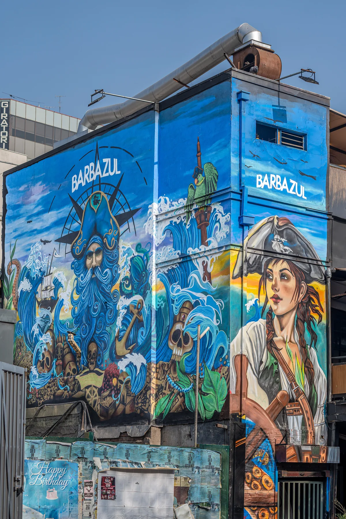A corner building covered in a blue mural of a bearded sailor and a woman in a hat.