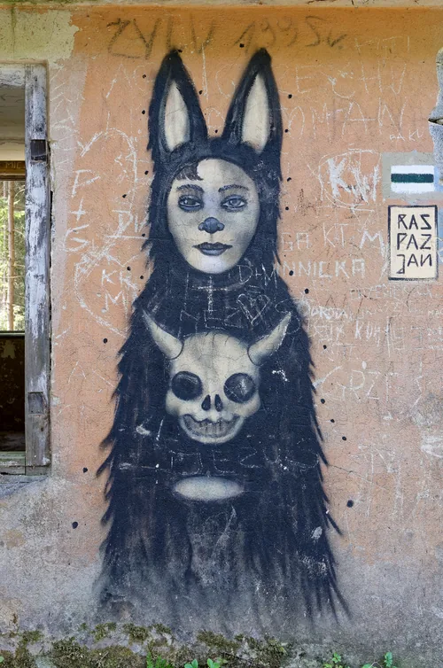 A graffiti figure with hare ears and a skull, painted in black on a weathered orange wall.
