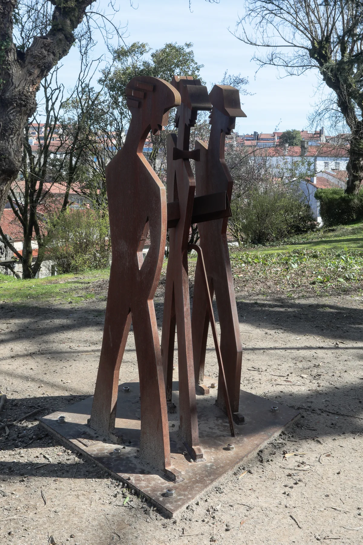 Flat rusted-steel silhouettes of figures standing together in a park.