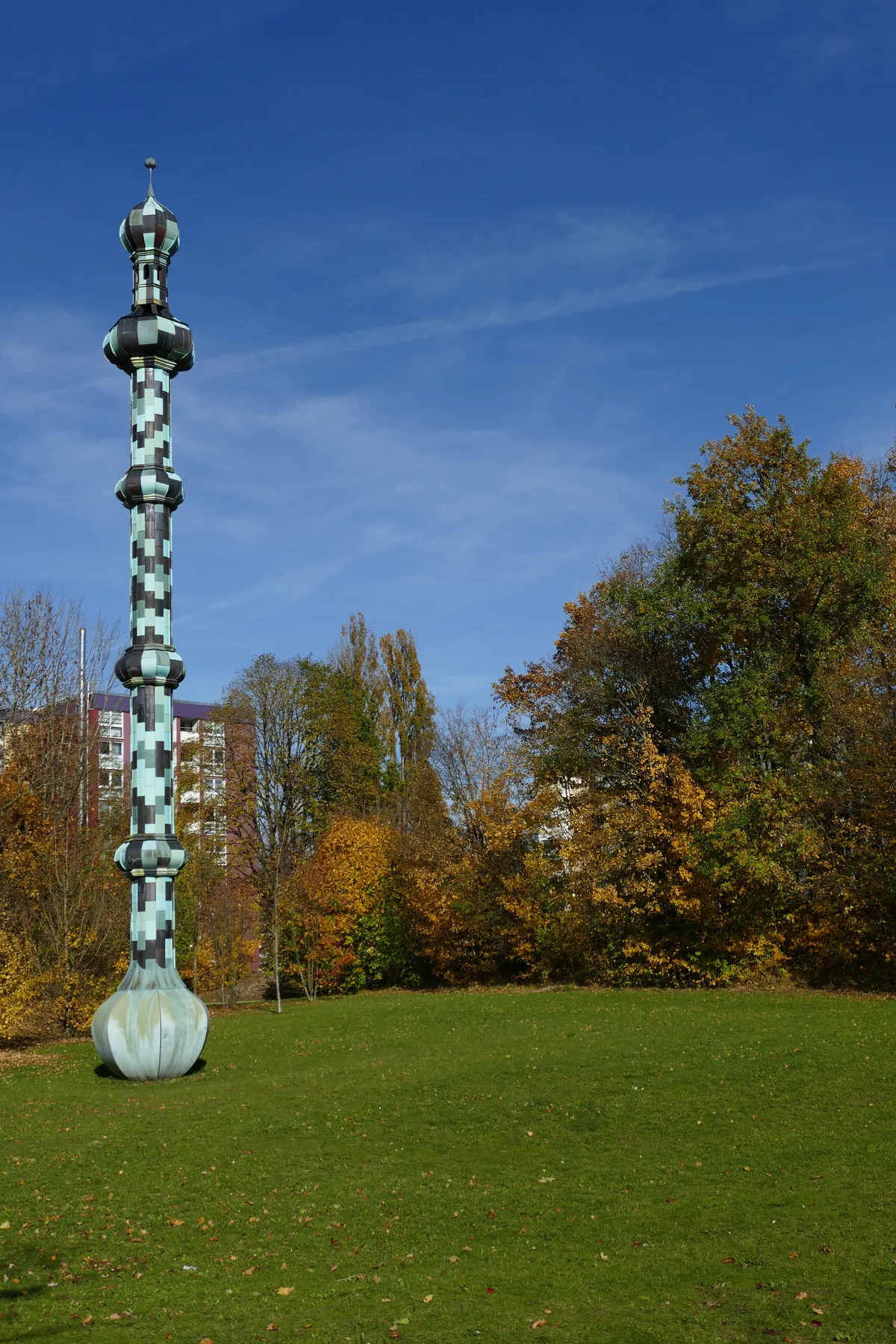 A tall stacked column of turned green and white forms rising from a meadow in autumn.
